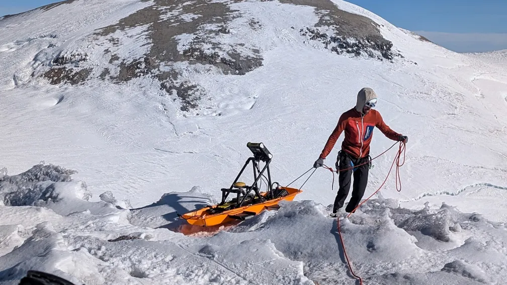 An individual owing a sled with a GPR unit on a snowy mountain landscape.