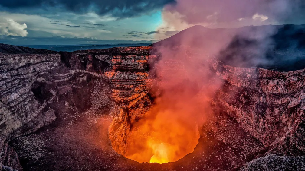 The active Santiago caldera of Volc&aacute;n Masaya giving off a plume of ash and glowing orange.