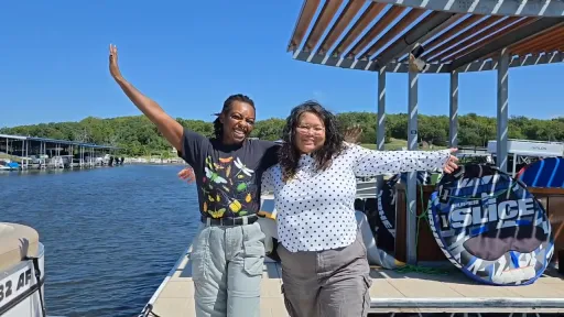 Two Geo-Launchpad interns stand on a boat, facing the camera and smiling with their arms out. Nikodemos "Nik" Scott is on the left, and Alana Jornacion is on the right.