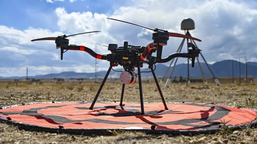Close photo of a drone on the ground with a GPS station and mountains in the background.