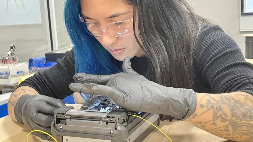 person wearing gloves carefully feeds cable into a box-shaped device