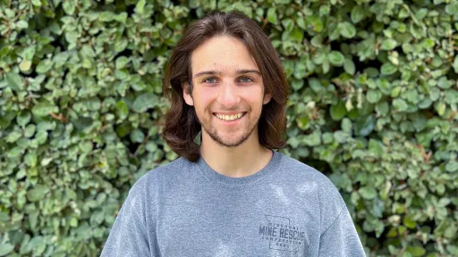 URISE intern Grant Clark smiling for a headshot with green foliage in the background.
