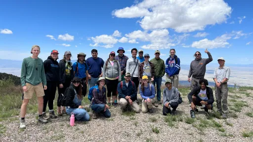 Group photo of two rows of students and instructional staff at the top of a mountain with big blue skies in the background.