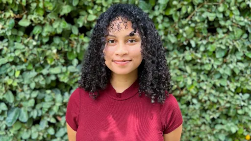 Natalie smiling for her headshot with green foliage in the background.