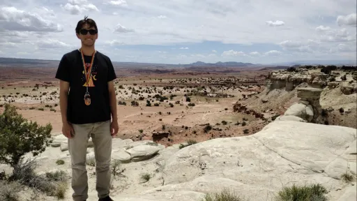 Intern Mario Coronado standing on rocks in the field while smiling at the camera. 