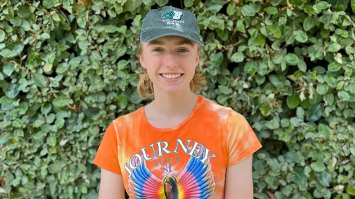 URISE intern Sarah Ayling smiling for a headshot with green foliage in the background.
