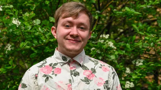 Kaden smiling for a headshot with green foliage behind him.