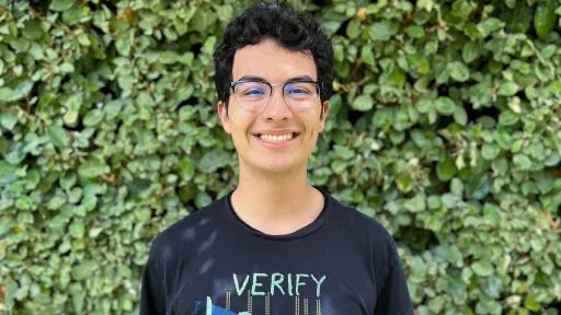URISE intern Yair Franco smiling for a headshot with green foliage in the background.