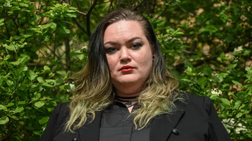 A headshot of Danielle wearing a grey collared shirt underneath a black blazer. 