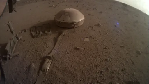 photo of the InSight seismometer sitting on the ground a few feet from the lander body, dusty ground surrounds and the horizon is curved in the fisheye lens view