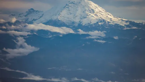 Aerial view of a volcano with the top covered in snow and surrounded by clouds.