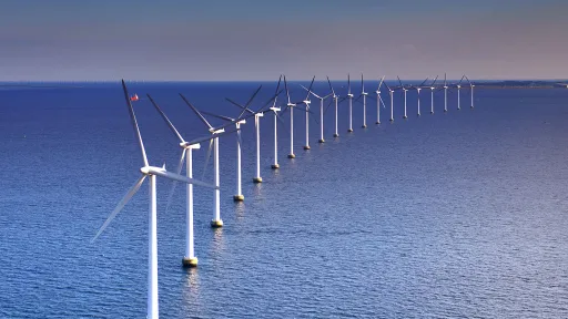 A row of offshore wind turbines curves toward the horizon over a calm sea.