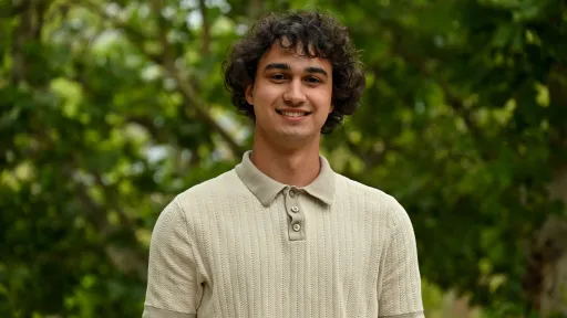 Headshot of Dylan wearing a collared short-sleeve shirt against a green foliage background