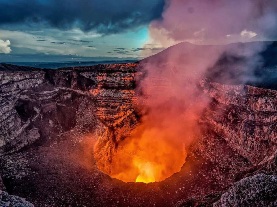 The active Santiago caldera of Volc&aacute;n Masaya giving off a plume of ash and glowing orange.