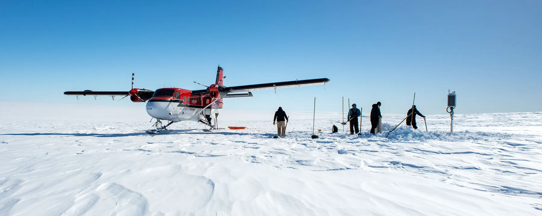 Engineers work next to a plane on the snow in Antarctica.