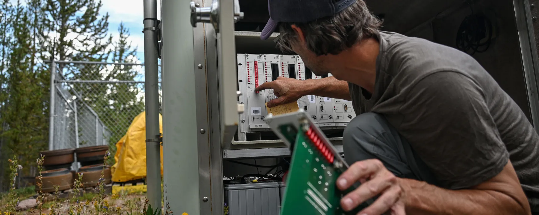 Engineer holds a circuit board while working on a borehole station in Yellowstone.