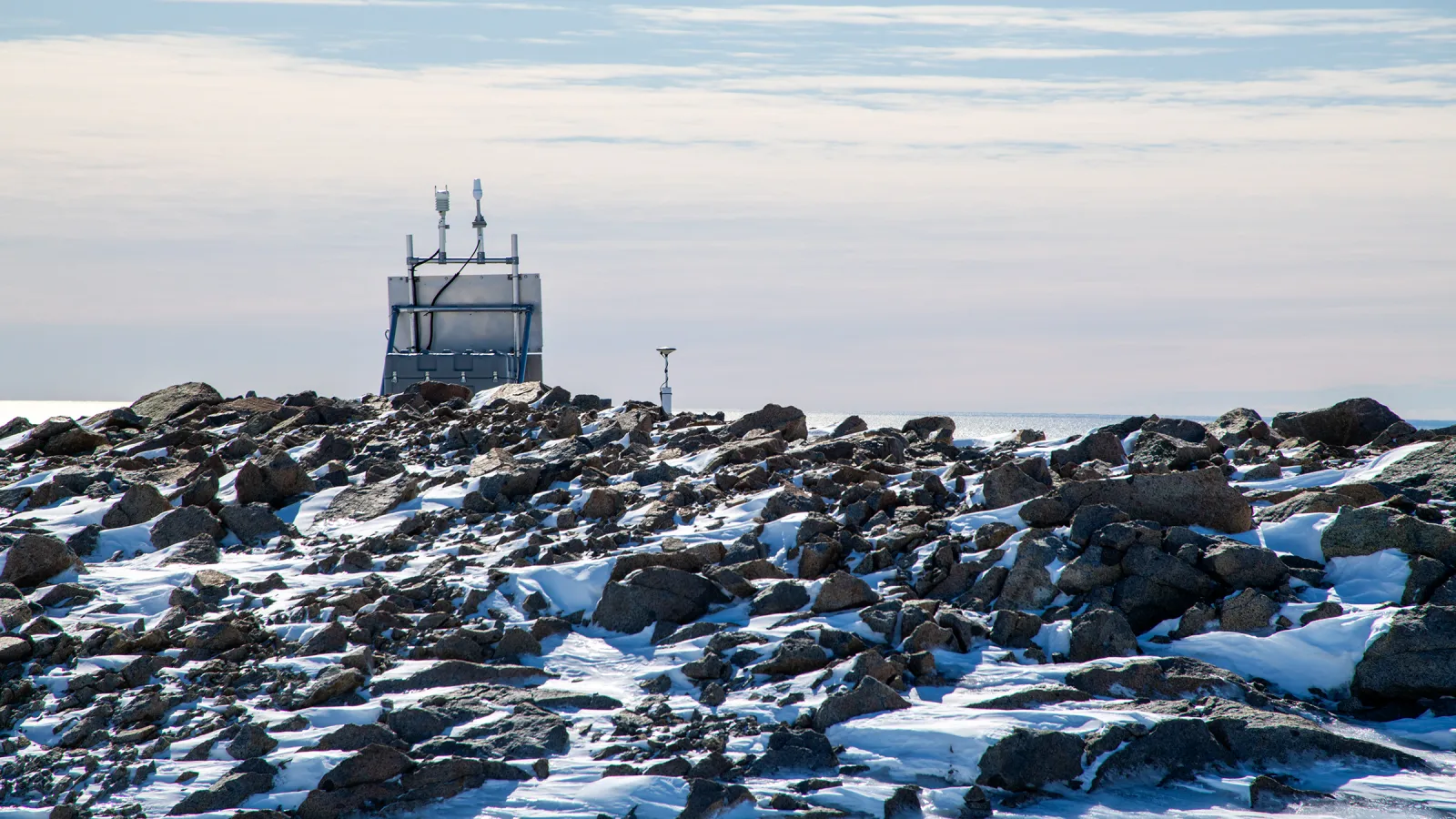 A GPS station in Antarctica with snow-covered rocks in the foreground.