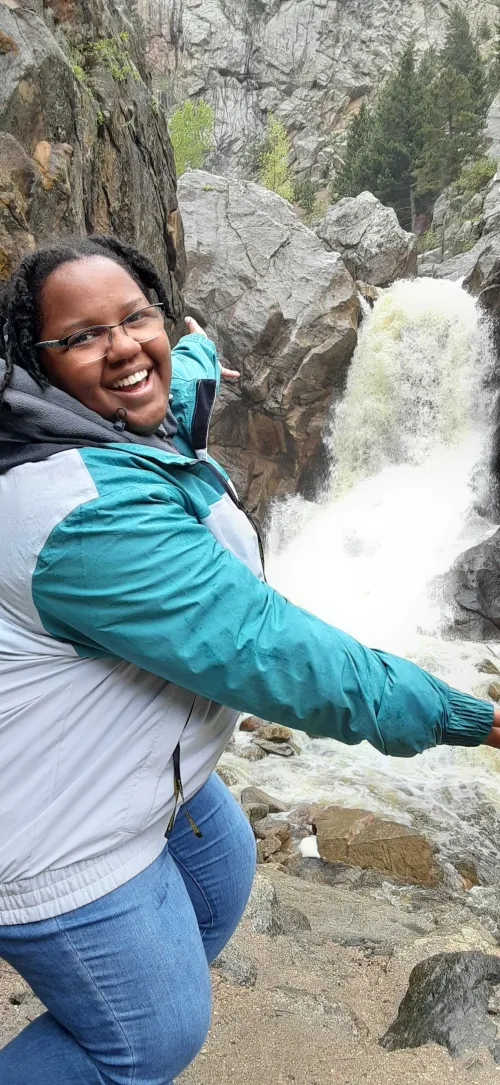 K.C. standing in front of a waterfall, smiling at the camera. 
