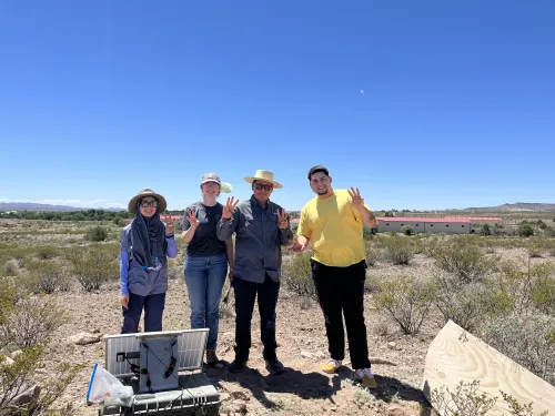 Elishua in the field with three others in a hat and sunglasses with three fingers raised.