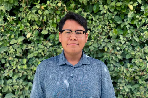 RESESS intern Elishua smilling for a headshot with green foliage in the background.