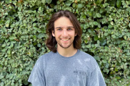 URISE intern Grant Clark smiling for a headshot with green foliage in the background.