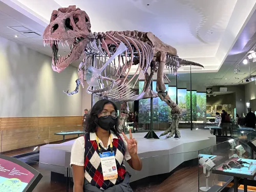 Shradha holding up a peace sign in front of a dinosaur fossil.