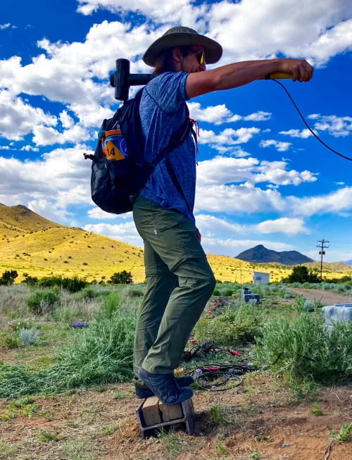 Grant Clark wearing a hat and sunglasses while working with seismic instruments in the field.
