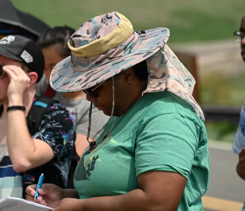 K.C. in a hat and glasses studying a paper in the field. 