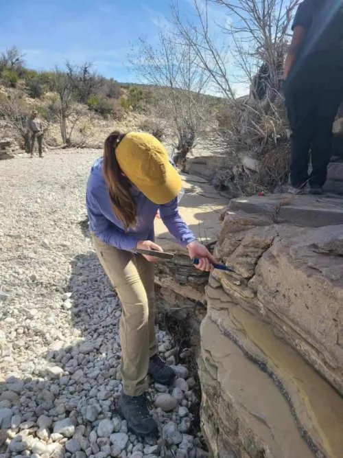 Anah wearing a yellow hat while working in the field on a rock outcrop.