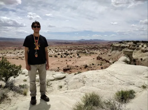 Intern Mario Coronado standing on rocks in the field while smiling at the camera. 