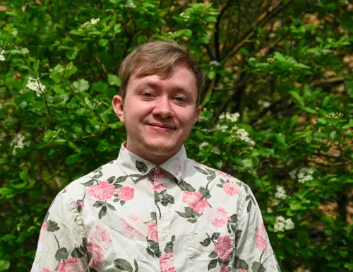 Kaden smiling for a headshot with green foliage behind him.