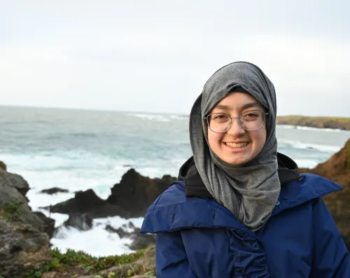 URISE intern Masooma Hasnain headshot in front of the ocean and rocks. 