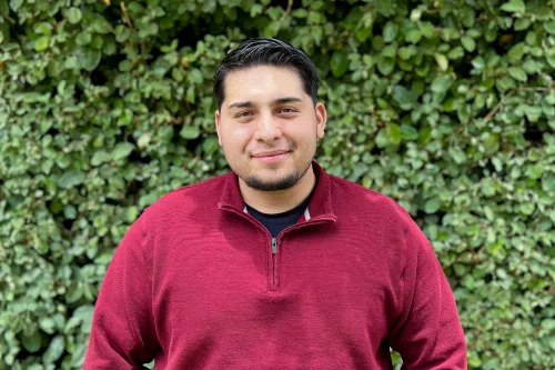Charles Garcia wearing a red quarter zip standing in front of a green leaf background smiling. 