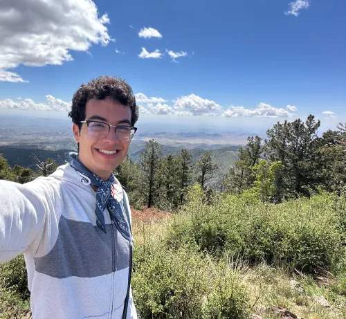 Yair smiling for a selfie with mountains and trees behind him.