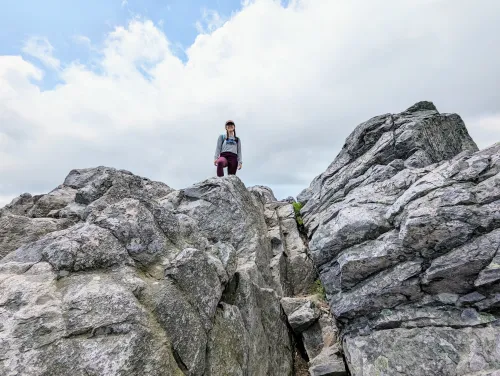 Isabella standing on rocks with a cloudy sky in the background. 