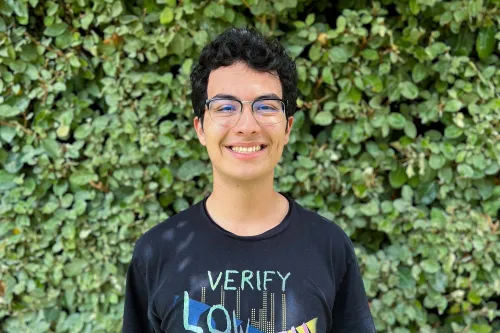 URISE intern Yair Franco smiling for a headshot with green foliage in the background.