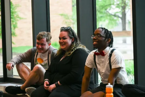 Danielle sitting on a windowsill laughing with two other interns 