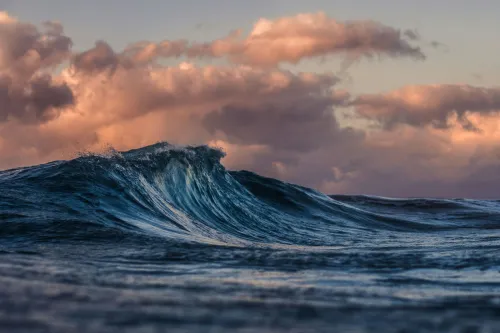 a gentle wave begins to crest, clouds and sunset in the sky behind