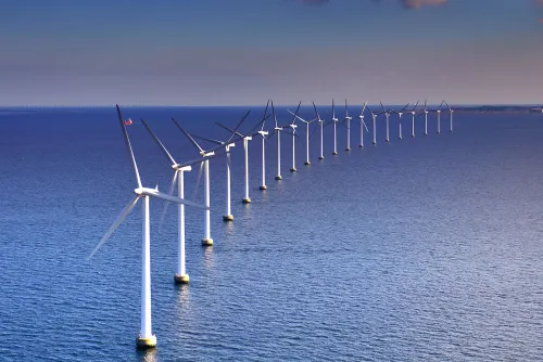 A row of offshore wind turbines curves toward the horizon over a calm sea.