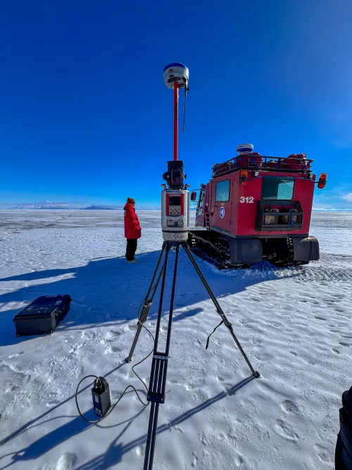 Terrestrial laser scanner atop a tripod, with a red box-shaped vehicle that rolls on tracks behind.