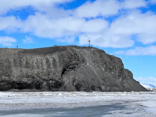 A gray, crumbly cliff rises from the sea ice, with a small cross visible on top.