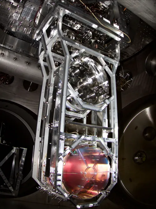 A set of circular mirrors hangs in an assembly within a metallic vacuum chamber.