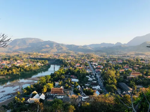 A photo overlooking a city with a river flowing through it, and  green mountains in the background.