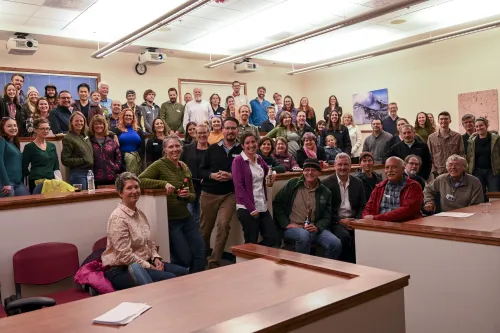 A large group of UNAVCO staff and community members gather for a celebratory group photo at the UNAVCO office in Boulder, Colorado, in October 2022. Smiling participants fill a tiered classroom space, some holding drinks, marking the organization&rsquo;s legacy ahead of its merger into EarthScope Consortium.