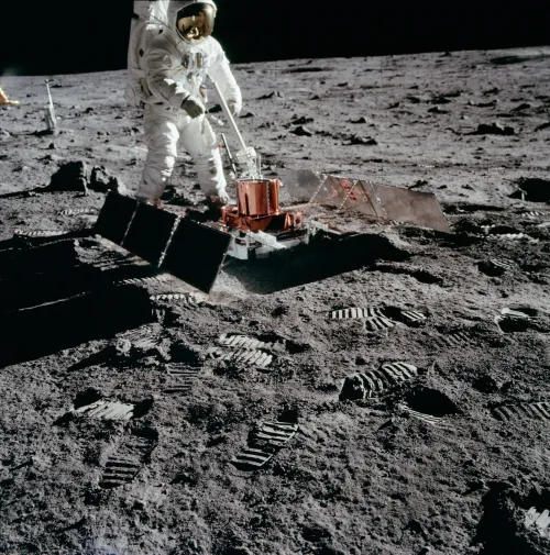 Photo of an astronaut deploying a sled-sized instrument with solar panels on either side.