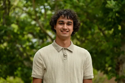 Headshot of Dylan wearing a collared short-sleeve shirt against a green foliage background