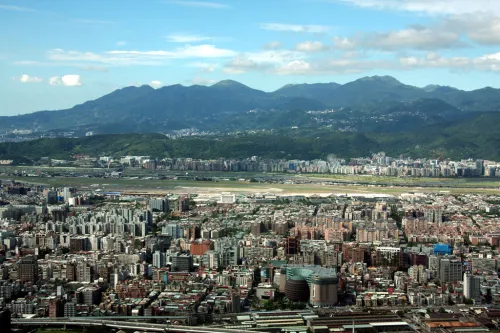 Photo overlooking a city full of multi-story buildings, with a row of lumpy peaks behind.
