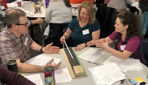 Three teachers at a table during a professional development workshop practicing with a hands-on activity that mimic earthquake behavior.